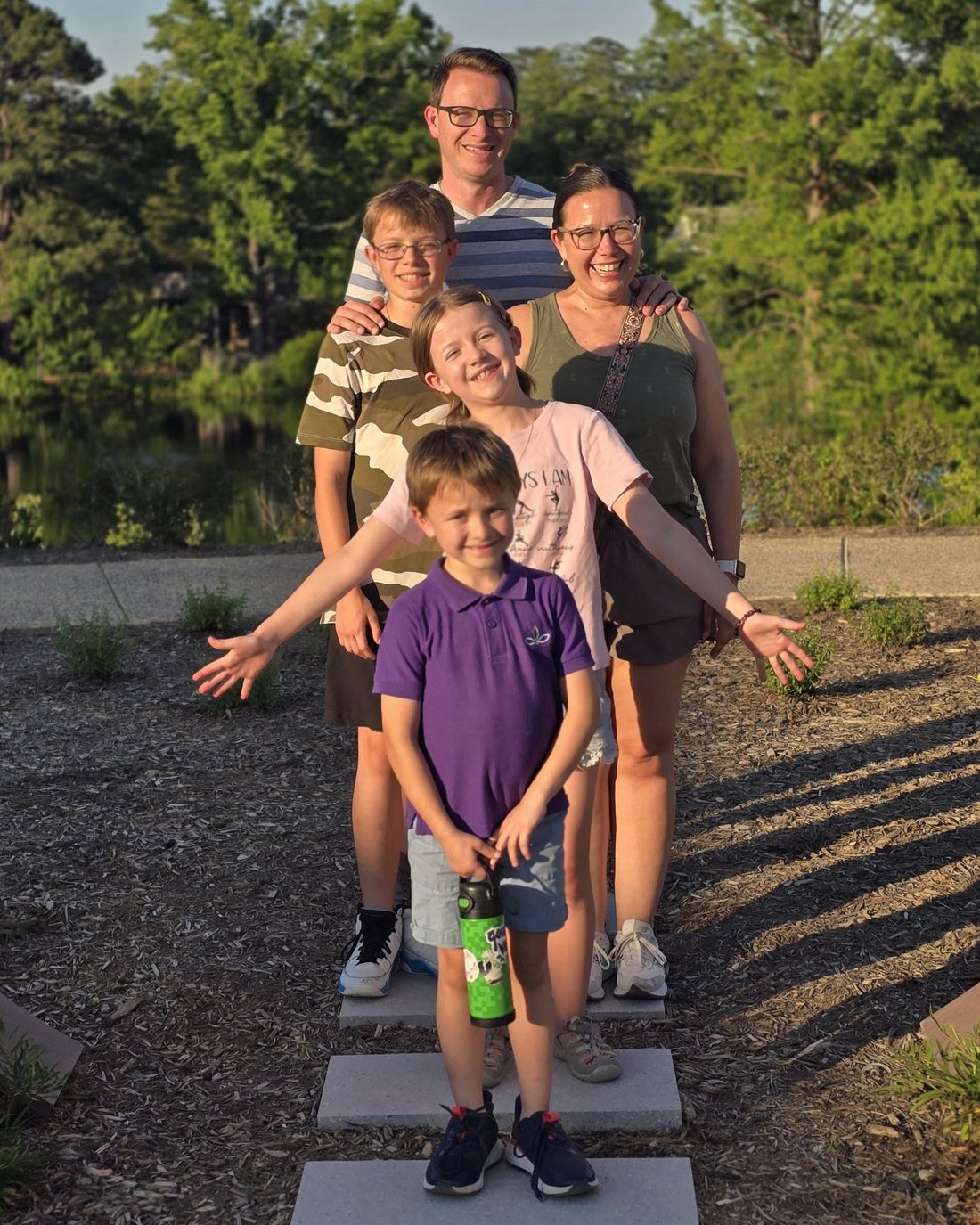 The Granger family smiling together on stepping stones beside a pond